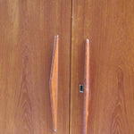 Armoire vintage en bois des années 60 avec deux portes, deux tiroirs, poignées sculptées et pieds compas.
