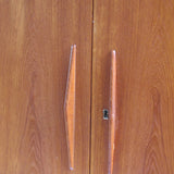 Armoire vintage en bois des années 60 avec deux portes, deux tiroirs, poignées sculptées et pieds compas.