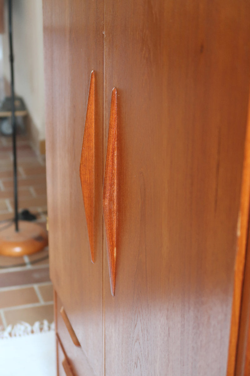 Armoire vintage en bois des années 60 avec deux portes, deux tiroirs, poignées sculptées et pieds compas.