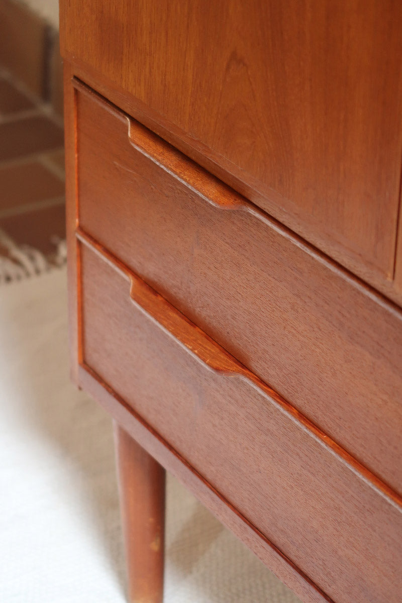 Armoire vintage en bois des années 60 avec deux portes, deux tiroirs, poignées sculptées et pieds compas.