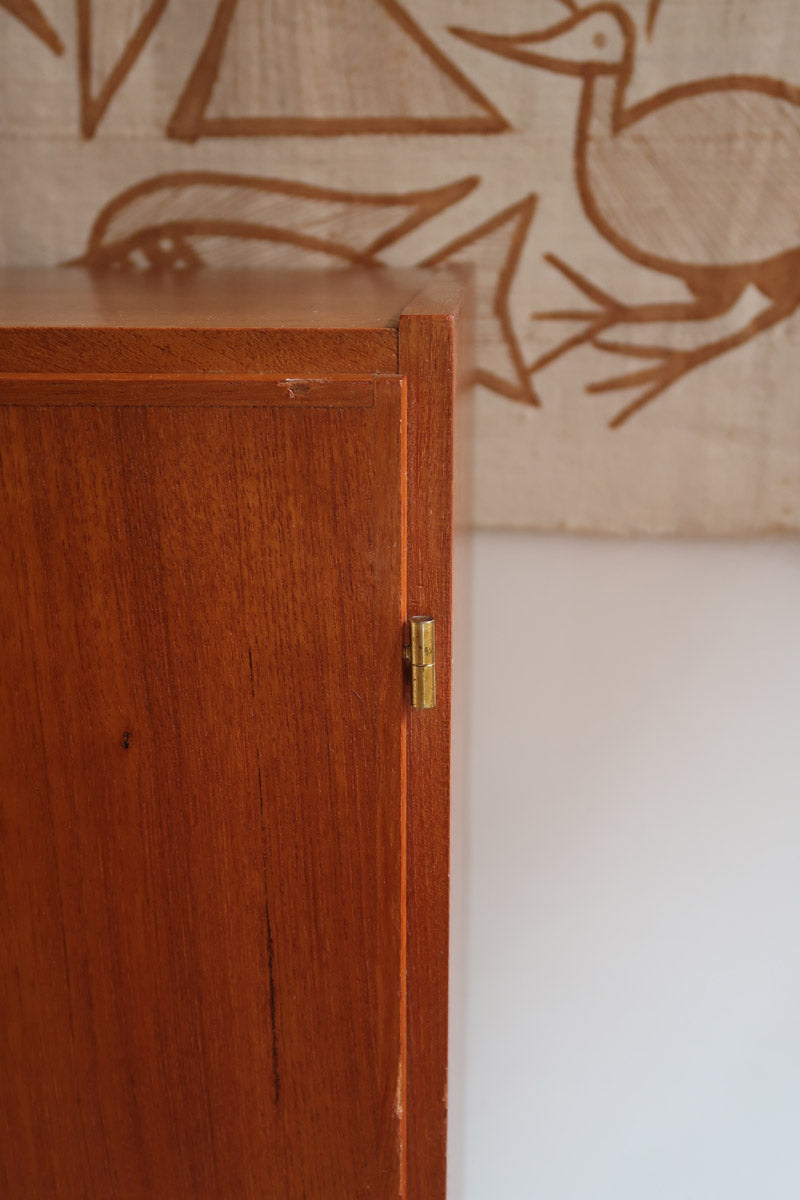Armoire vintage en bois des années 60 avec deux portes, deux tiroirs, poignées sculptées et pieds compas.