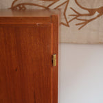 Armoire vintage en bois des années 60 avec deux portes, deux tiroirs, poignées sculptées et pieds compas.