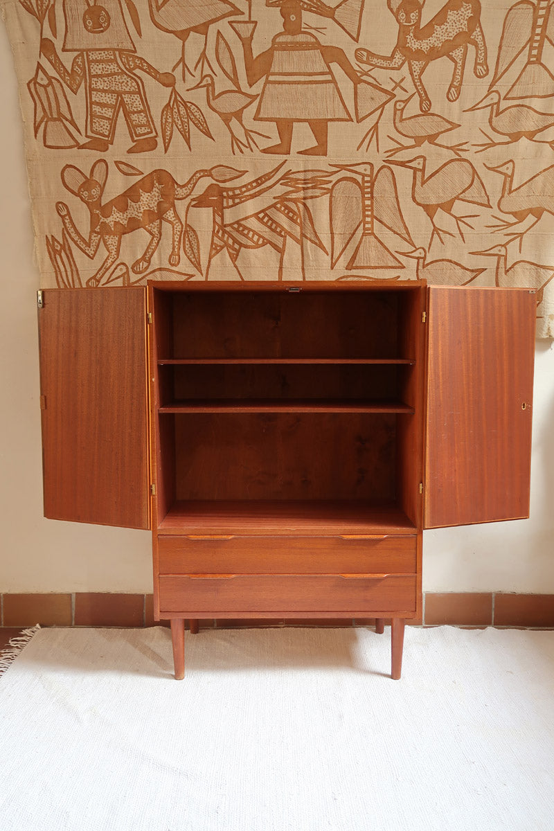 Armoire vintage en bois des années 60 avec deux portes, deux tiroirs, poignées sculptées et pieds compas.