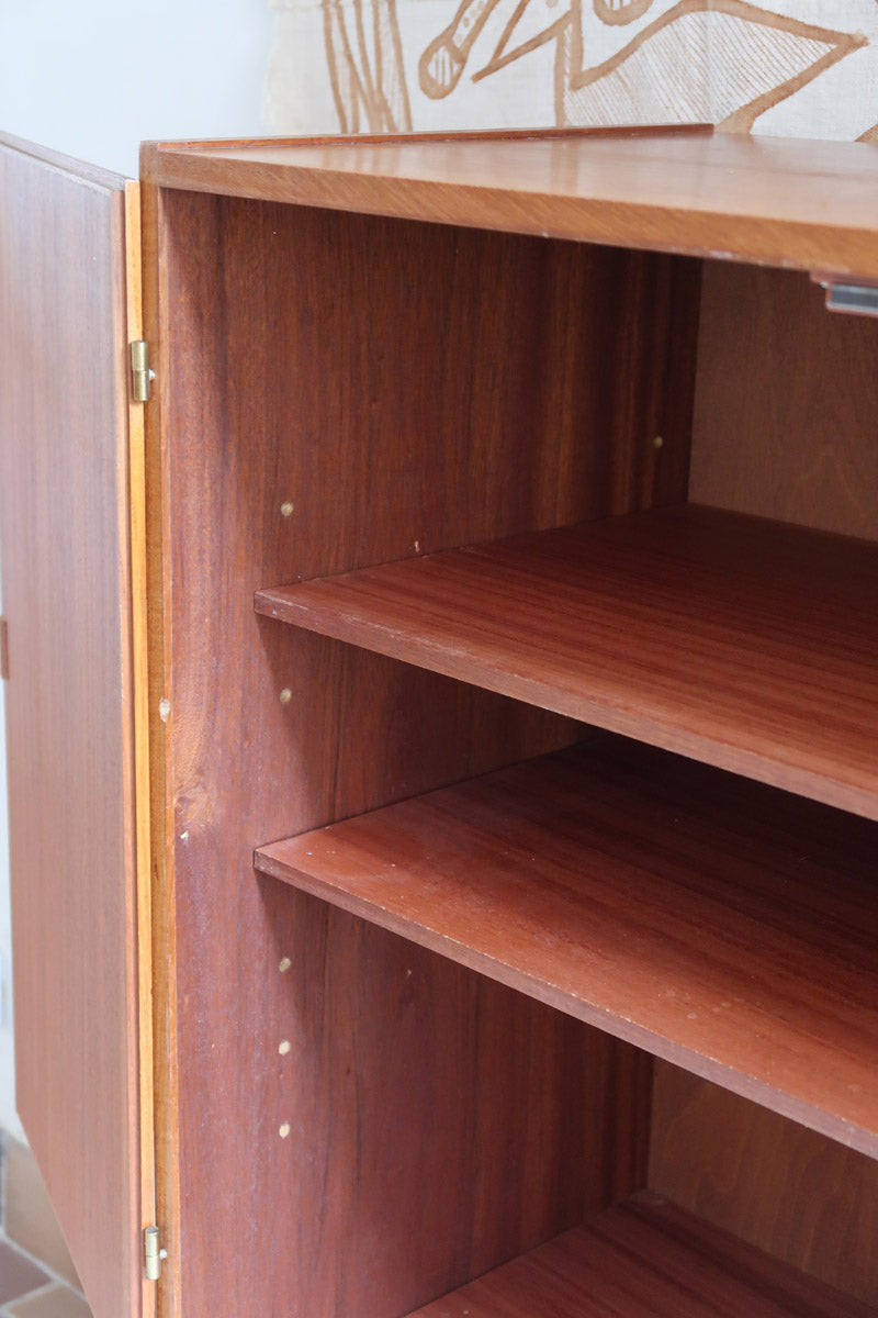 Armoire vintage en bois des années 60 avec deux portes, deux tiroirs, poignées sculptées et pieds compas.