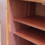 Armoire vintage en bois des années 60 avec deux portes, deux tiroirs, poignées sculptées et pieds compas.