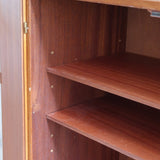 Armoire vintage en bois des années 60 avec deux portes, deux tiroirs, poignées sculptées et pieds compas.