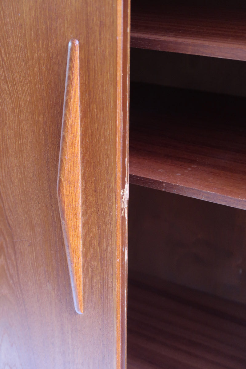 Armoire vintage en bois des années 60 avec deux portes, deux tiroirs, poignées sculptées et pieds compas.