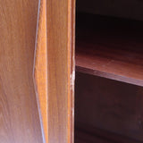 Armoire vintage en bois des années 60 avec deux portes, deux tiroirs, poignées sculptées et pieds compas.