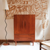 Armoire vintage en bois des années 60 avec deux portes, deux tiroirs, poignées sculptées et pieds compas.
