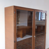 Bibliothèque vitrée vintage en bois de noyer, années 60, esprit Art déco, deux portes vitrées à encadrement de bois fermant à clé, quatre tablettes réglables, socle débordant à gradins sur deux patins pleins