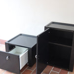 Duo de caissons vintage Roche Bobois années 90, bois laqué noir, module haut à abattant et module cube à porte, poignées chromées encastrées, intérieur laqué blanc