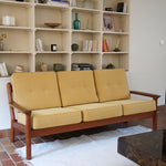 Canapé 3 places scandinave en teck des années 60 avec coussins en tissu jaune moutarde et structure type banquette.