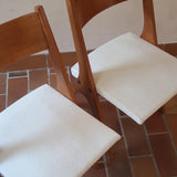 Deux chaises vintage en hêtre massif des années 50 avec assise en tissu bouclette clair, design épuré à la René-Jean Caillette, présentées seules et en mise en situation.