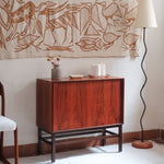 Buffet scandinave en teck années 60 à porte coulissante latérale, piètement foncé et intérieur ouvert.