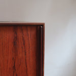 Buffet scandinave en teck années 60 à porte coulissante latérale, piètement foncé et intérieur ouvert.