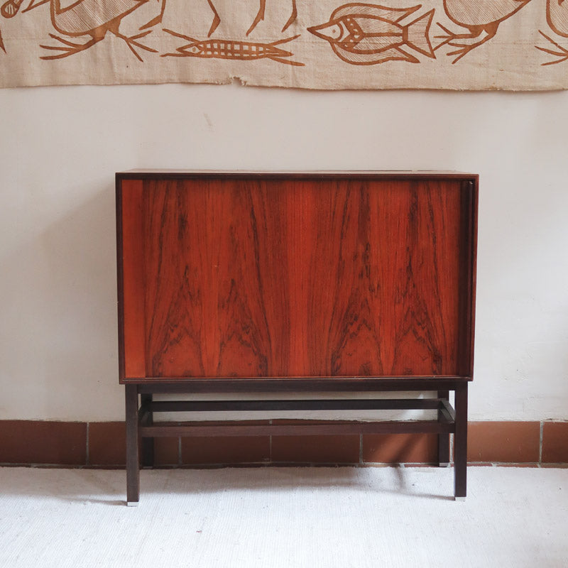 Buffet scandinave en teck années 60 à porte coulissante latérale, piètement foncé et intérieur ouvert.