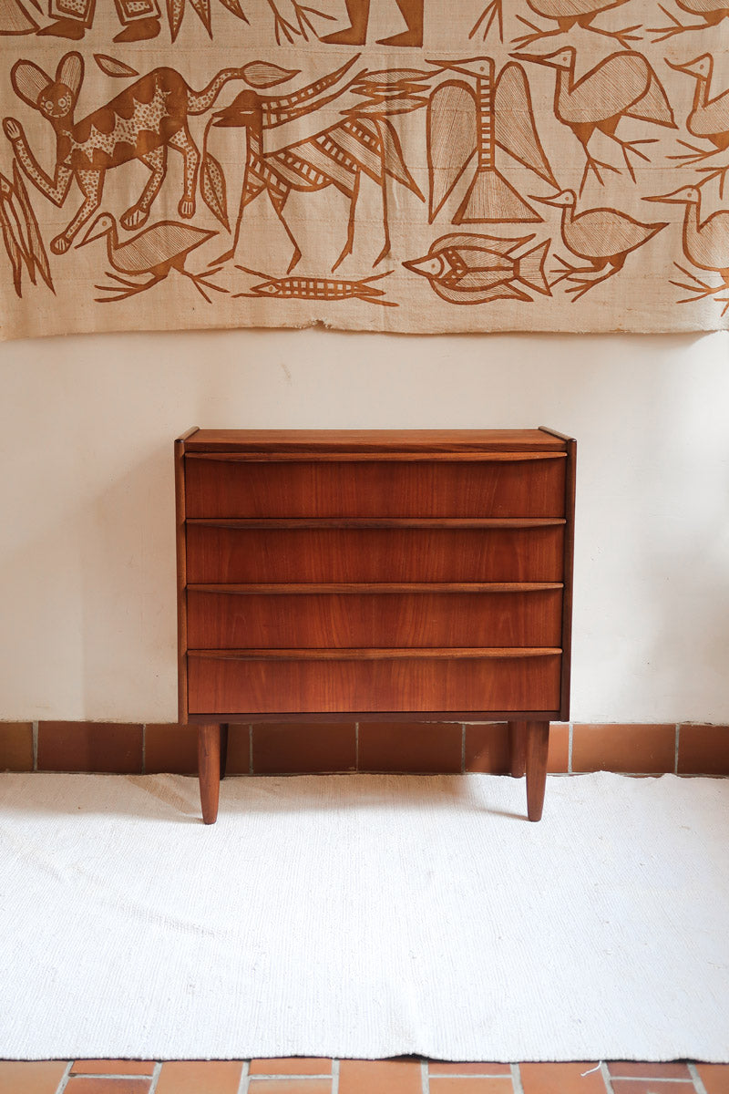 Commode vintage en teck des années 60 avec quatre tiroirs, façades galbées, poignées intégrées et pieds compas.