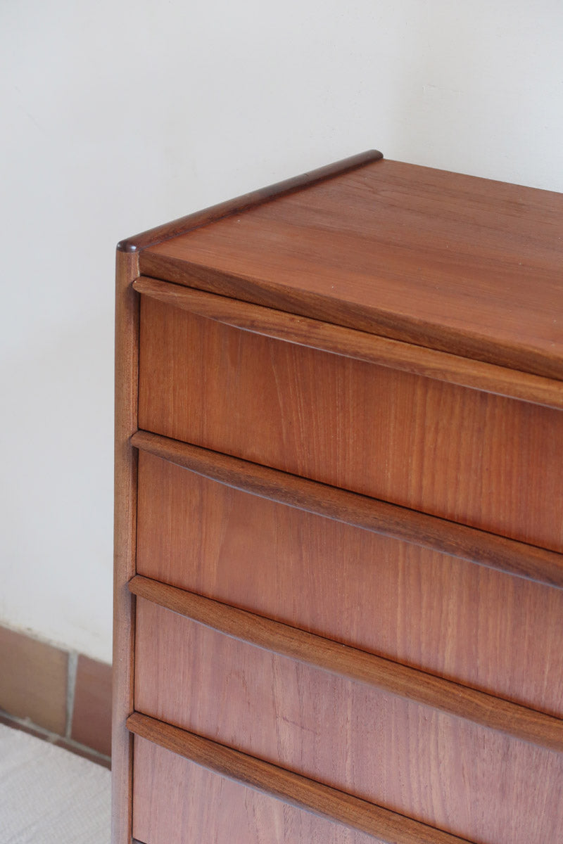 Commode vintage en teck des années 60 avec quatre tiroirs, façades galbées, poignées intégrées et pieds compas.