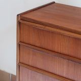 Commode vintage en teck des années 60 avec quatre tiroirs, façades galbées, poignées intégrées et pieds compas.