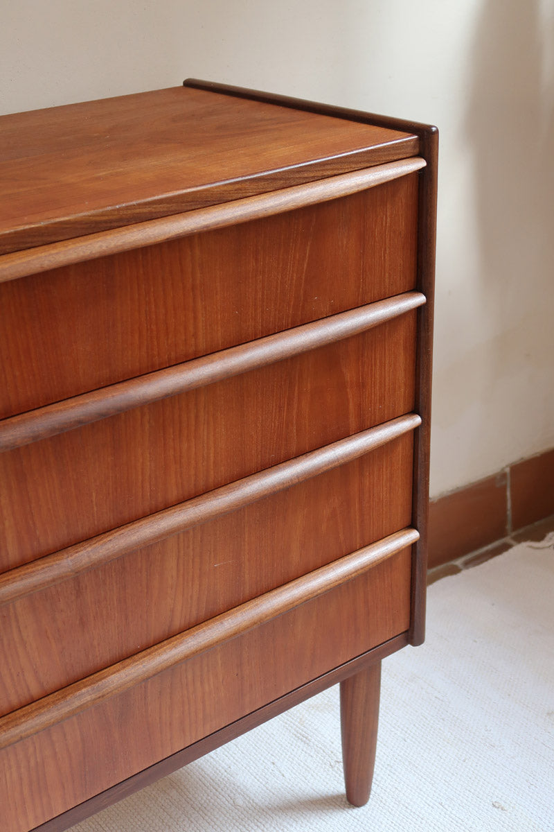 Commode vintage en teck des années 60 avec quatre tiroirs, façades galbées, poignées intégrées et pieds compas.