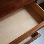 Commode vintage en teck des années 60 avec quatre tiroirs, façades galbées, poignées intégrées et pieds compas.