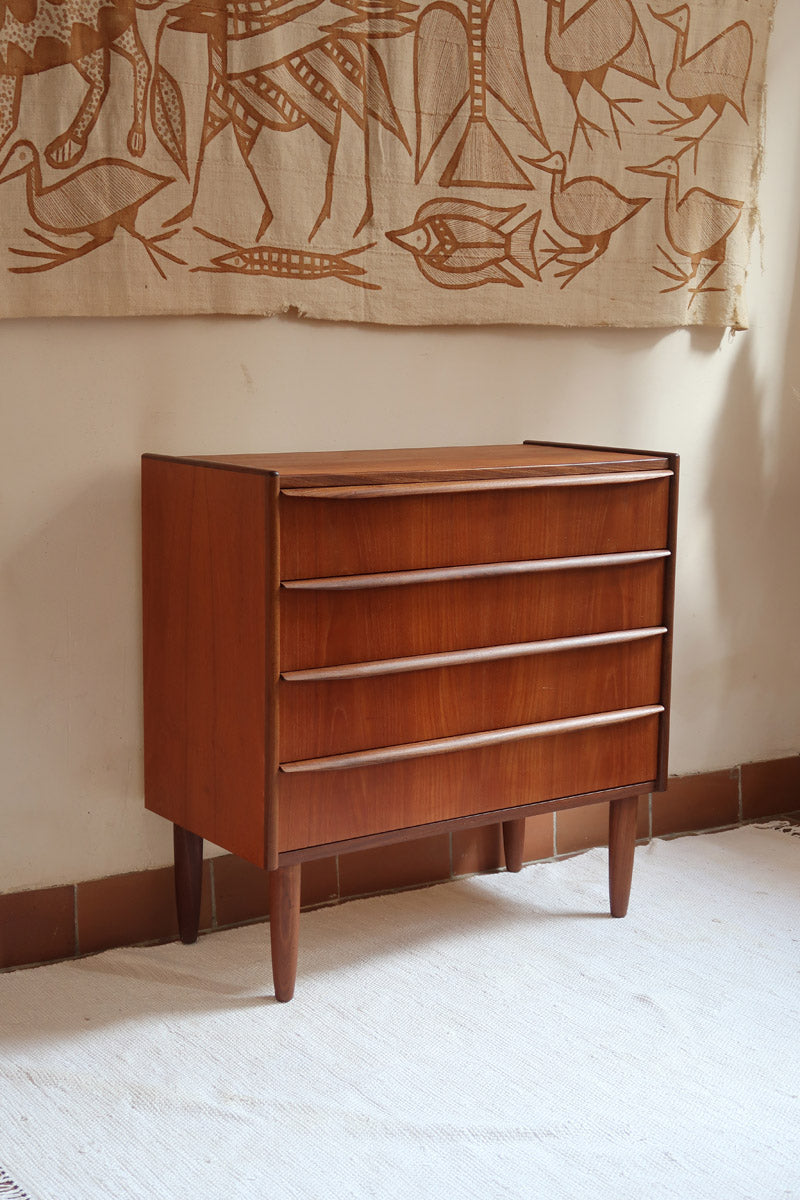 Commode vintage en teck des années 60 avec quatre tiroirs, façades galbées, poignées intégrées et pieds compas.