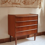 Commode vintage en teck des années 60 avec quatre tiroirs, façades galbées, poignées intégrées et pieds compas.