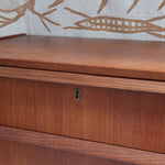 Commode scandinave en teck années 60 à cinq tiroirs, poignées sculptées intégrées et pieds compas.