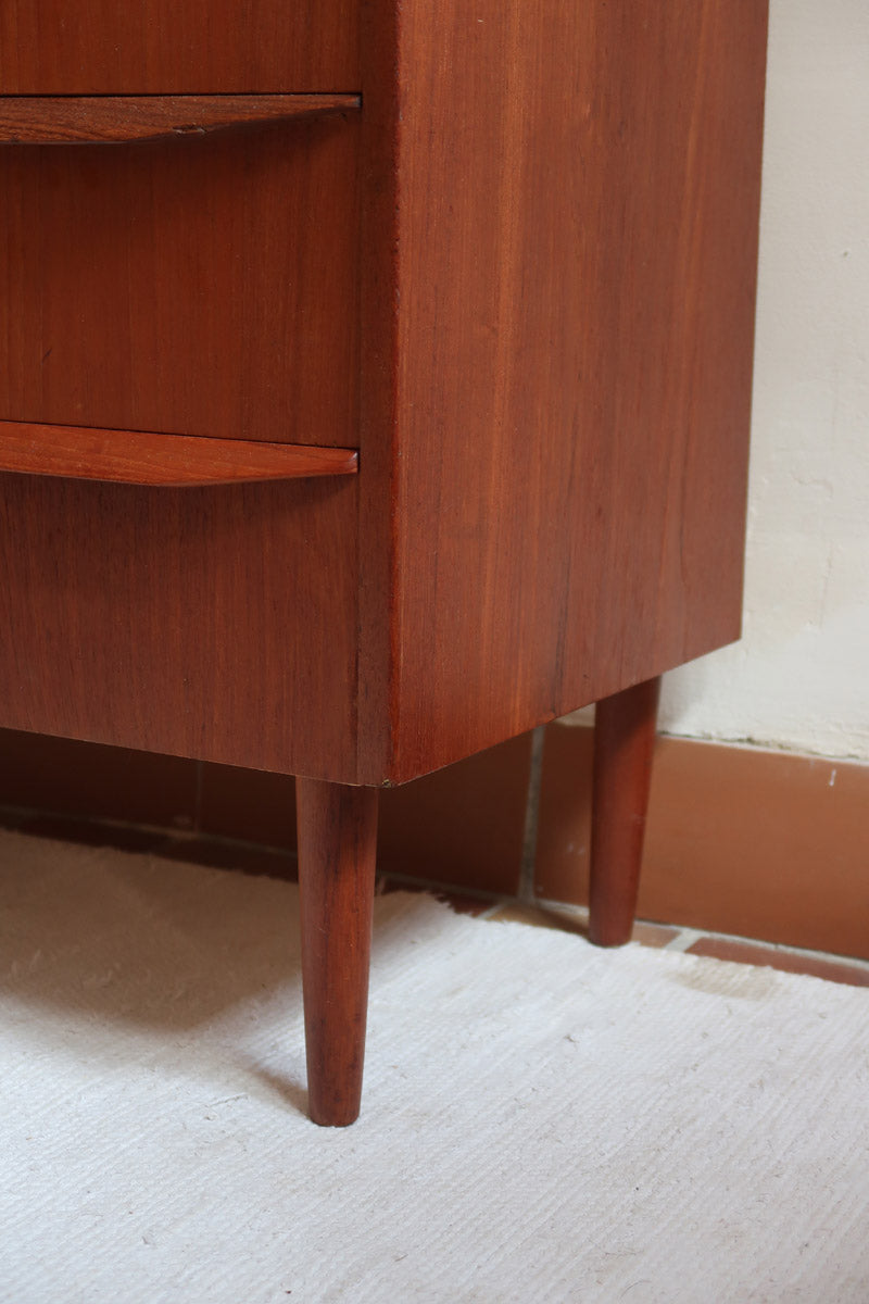 Commode scandinave en teck années 60 à cinq tiroirs, poignées sculptées intégrées et pieds compas.