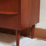 Commode scandinave en teck années 60 à cinq tiroirs, poignées sculptées intégrées et pieds compas.
