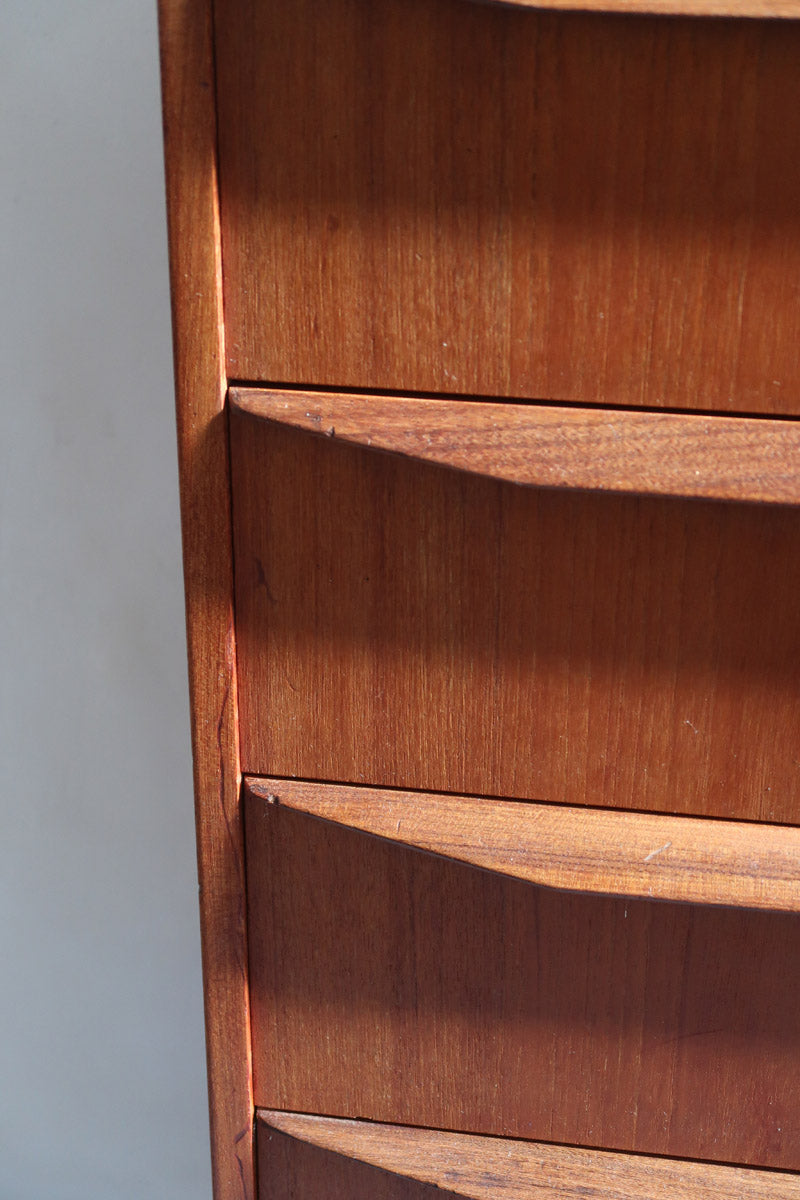 Commode scandinave en teck années 60 à cinq tiroirs, poignées sculptées intégrées et pieds compas.