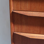 Commode scandinave en teck années 60 à cinq tiroirs, poignées sculptées intégrées et pieds compas.