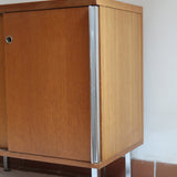 Meuble bas années 70 en bois avec piètement et montants en métal chromé, portes coulissantes et étagère intérieure.