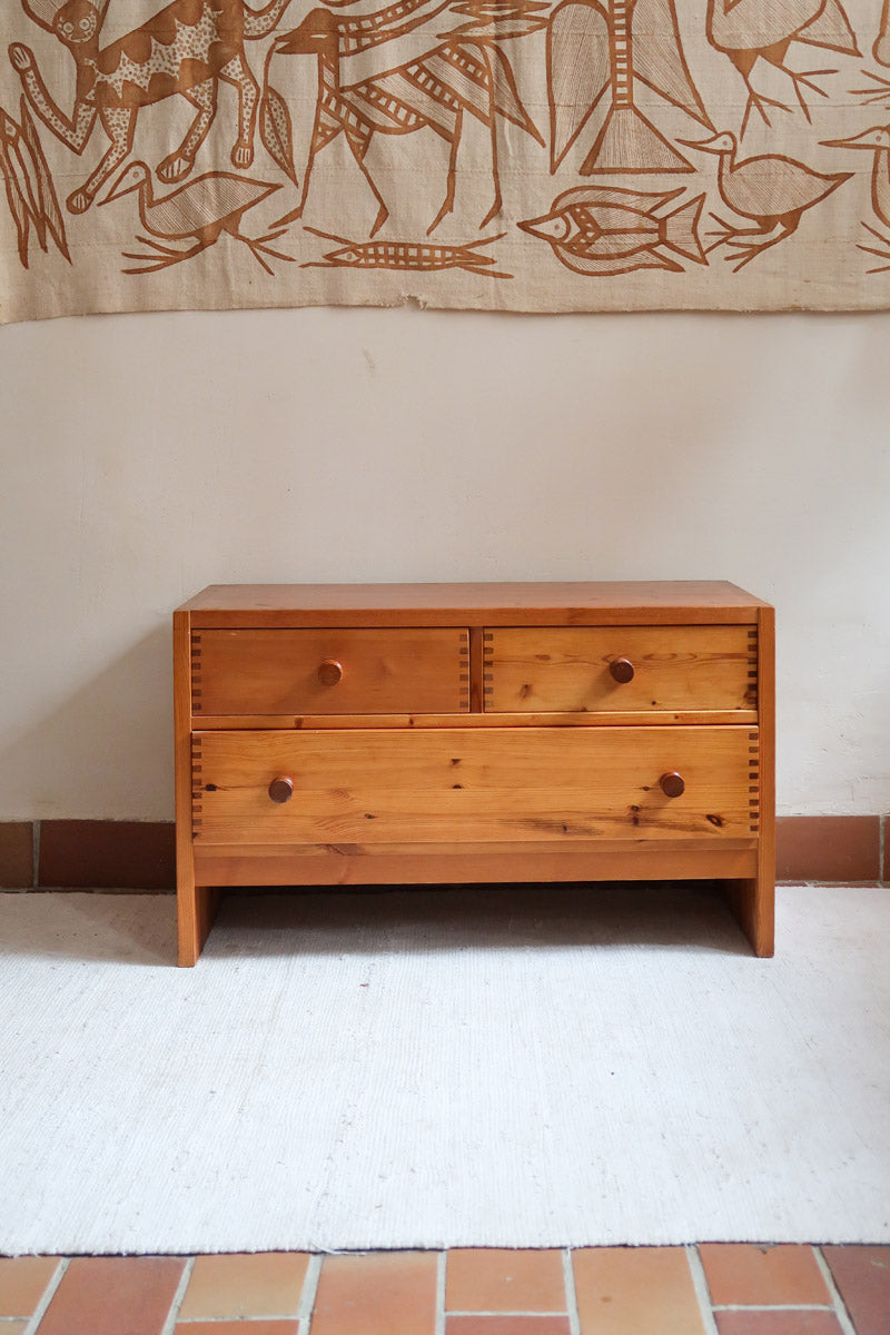 Commode basse en pin massif années 70 à trois tiroirs avec assemblages à queues d’aronde visibles et poignées rondes en bois.