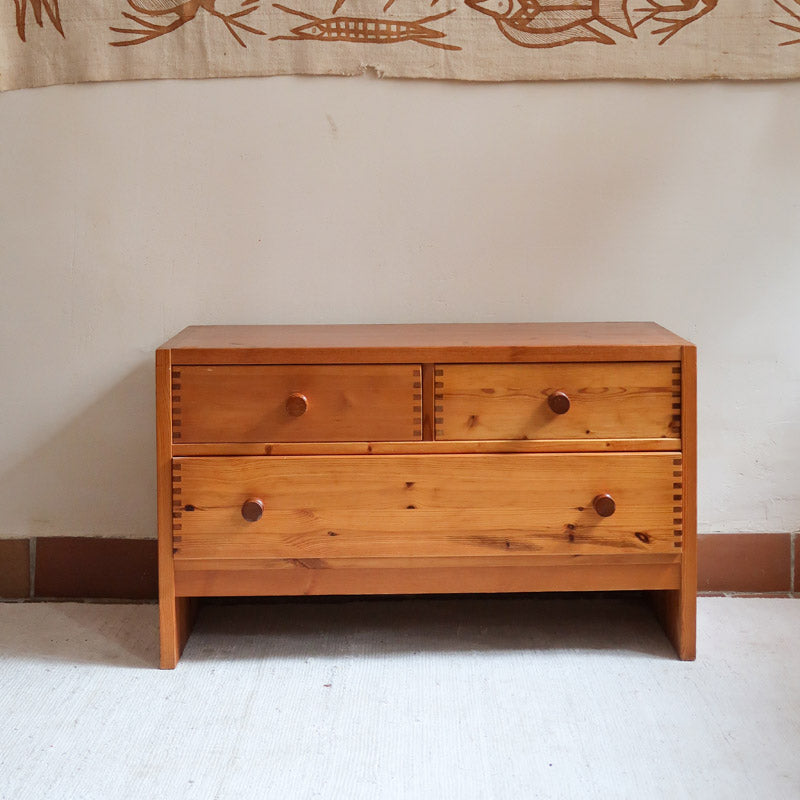 Commode basse en pin massif années 70 à trois tiroirs avec assemblages à queues d’aronde visibles et poignées rondes en bois.