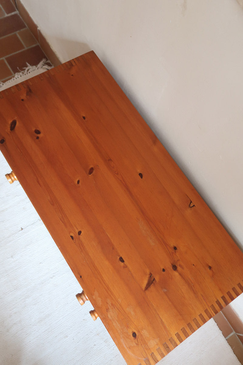Commode basse en pin massif années 70 à trois tiroirs avec assemblages à queues d’aronde visibles et poignées rondes en bois.
