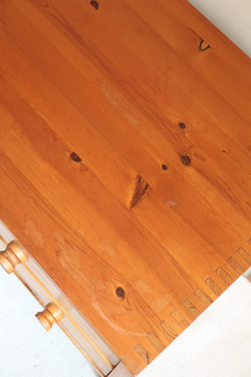 Commode basse en pin massif années 70 à trois tiroirs avec assemblages à queues d’aronde visibles et poignées rondes en bois.