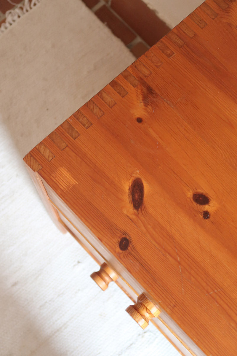 Commode basse en pin massif années 70 à trois tiroirs avec assemblages à queues d’aronde visibles et poignées rondes en bois.