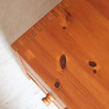 Commode basse en pin massif années 70 à trois tiroirs avec assemblages à queues d’aronde visibles et poignées rondes en bois.
