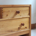 Commode basse en pin massif années 70 à trois tiroirs avec assemblages à queues d’aronde visibles et poignées rondes en bois.