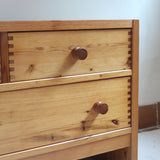 Commode basse en pin massif années 70 à trois tiroirs avec assemblages à queues d’aronde visibles et poignées rondes en bois.