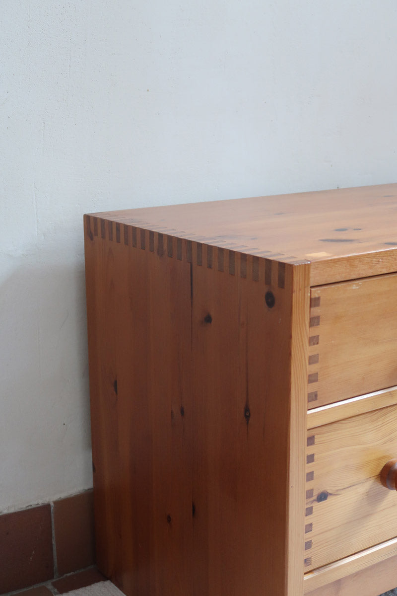 Commode basse en pin massif années 70 à trois tiroirs avec assemblages à queues d’aronde visibles et poignées rondes en bois.