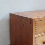 Commode basse en pin massif années 70 à trois tiroirs avec assemblages à queues d’aronde visibles et poignées rondes en bois.
