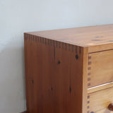 Commode basse en pin massif années 70 à trois tiroirs avec assemblages à queues d’aronde visibles et poignées rondes en bois.