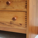Commode basse en pin massif années 70 à trois tiroirs avec assemblages à queues d’aronde visibles et poignées rondes en bois.