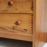 Commode basse en pin massif années 70 à trois tiroirs avec assemblages à queues d’aronde visibles et poignées rondes en bois.