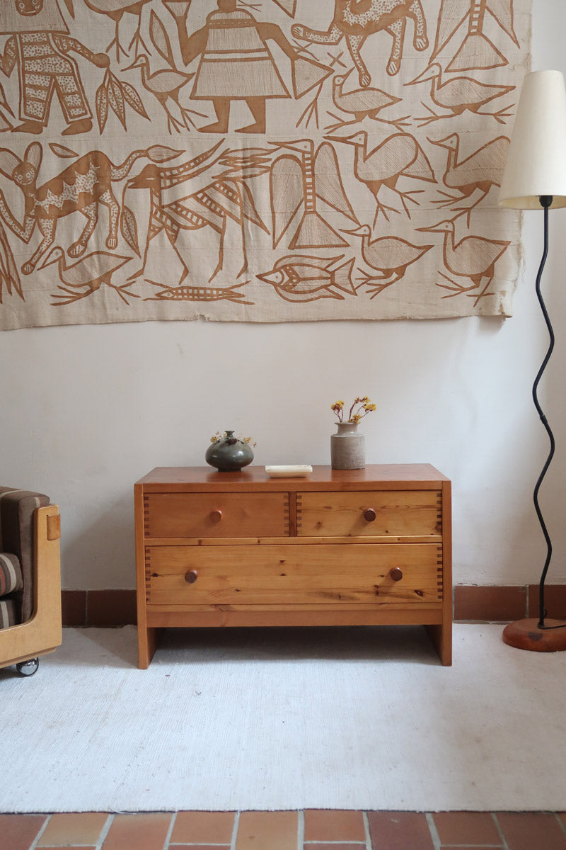 Commode basse en pin massif années 70 à trois tiroirs avec assemblages à queues d’aronde visibles et poignées rondes en bois.