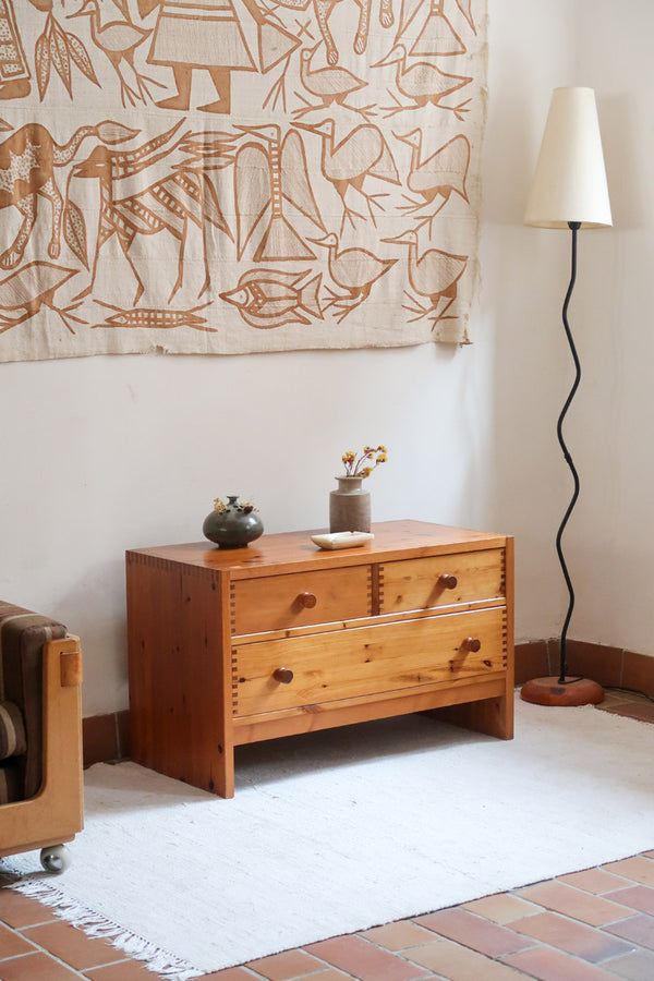 Commode basse en pin massif années 70 à trois tiroirs avec assemblages à queues d’aronde visibles et poignées rondes en bois.