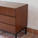 Commode vintage 3 tiroirs en teck années 60, façades pleines à prise de main creusée, piétement fin en métal laqué noir, style scandinave