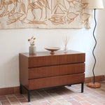 Commode vintage 3 tiroirs en teck années 60, façades pleines à prise de main creusée, piétement fin en métal laqué noir, style scandinave